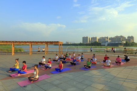 Foto de CONDADO DE LUANNAN, China - 30 de junio de 2018: Las mujeres practican yoga al aire libre en un parque, CONDADO DE LUANNAN, provincia de Hebei, China - Imagen libre de derechos