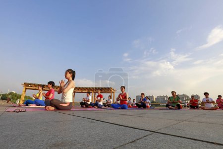 Foto de CONDADO DE LUANNAN, China - 30 de junio de 2018: Las mujeres practican yoga al aire libre en un parque, CONDADO DE LUANNAN, provincia de Hebei, China - Imagen libre de derechos