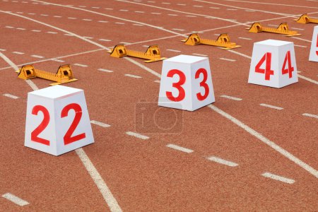 Téléchargez les photos : Numéros de piste et démarreurs sur la piste en plastique sur le terrain de jeu - en image libre de droit