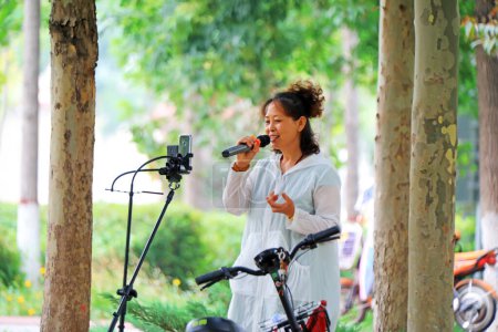 Photo for Luannan County, China - July 5, 2019: A lady sings in the park, Luannan County, Hebei Province, China. - Royalty Free Image