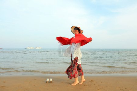 Foto de LUANNAN COUNTY, provincia de Hebei, China - 3 de mayo de 2019: Una dama con un chal rojo está jugando junto al mar. - Imagen libre de derechos