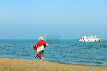 Téléchargez les photos : Une dame en rouge joue au bord de la mer, en Chine du Nord - en image libre de droit