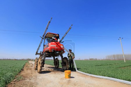 Photo for Luannan County - April 10, 2019: Technicians pour water into the self propelled boom sprayer on a farm, Luannan County, Hebei Province, Chin - Royalty Free Image