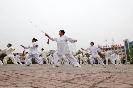 Foto de CONDADO DE LUANNAN, provincia de Hebei, China - 29 de abril de 2019: la gente practica la espada Tai Chi en la plaza del parque. - Imagen libre de derechos