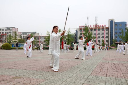 Foto de CONDADO DE LUANNAN, provincia de Hebei, China - 29 de abril de 2019: la gente practica la espada Tai Chi en la plaza del parque. - Imagen libre de derechos