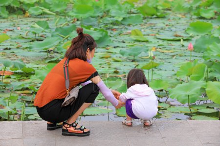 Téléchargez les photos : Quelques mères et filles regardent des fleurs de lotus près d'un étang dans un parc, comté de Luannan, province du Hebei, Chine - en image libre de droit
