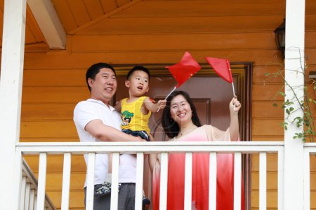 Photo for Luannan County, China - July 5, 2019: A family of three singing on a fence upstairs waving the Chinese national flag, Luannan County, Hebei Province, China. - Royalty Free Image