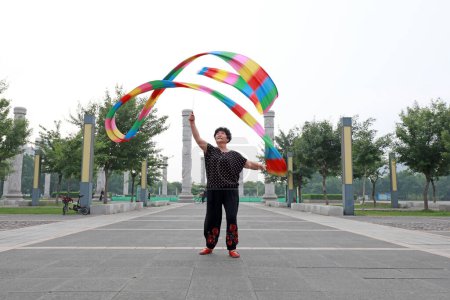 Téléchargez les photos : Comté de Luannan, Chine - 9 juillet 2019 : Des gens agitent des rubans pour faire de l'exercice dans les parcs, comté de Luannan, province du Hebei, Chine. De nos jours, beaucoup de Chinois attachent une grande importance à l'exercice physique. - en image libre de droit