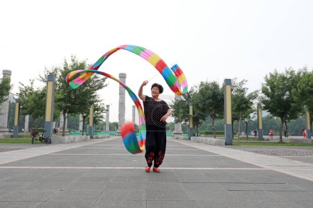 Téléchargez les photos : Comté de Luannan, Chine - 9 juillet 2019 : Des gens agitent des rubans pour faire de l'exercice dans les parcs, comté de Luannan, province du Hebei, Chine. De nos jours, beaucoup de Chinois attachent une grande importance à l'exercice physique. - en image libre de droit