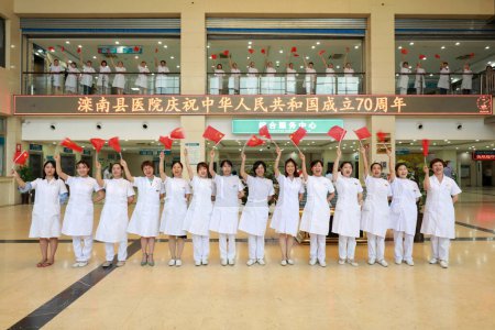Foto de Condado de Luannan, China - 9 de julio de 2019: Un grupo de trabajadores médicos cantaba con la bandera nacional en la mano, Condado de Luannan, provincia de Hebei, China. - Imagen libre de derechos