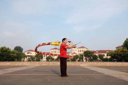 Foto de Condado de Luannan, China - 11 de julio de 2019: La gente agita Diabolo Dragon para ejercitarse en parques, Condado de Luannan, provincia de Hebei, China. Diabolo Dragon es una de las formas tradicionales de fitness popular chino. - Imagen libre de derechos
