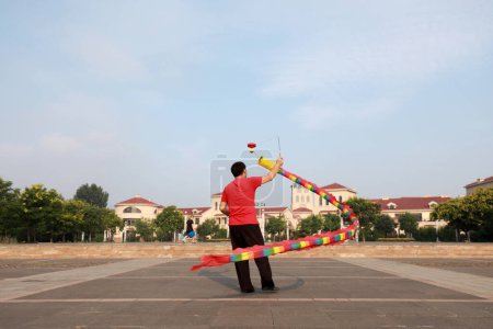 Foto de Condado de Luannan, China - 11 de julio de 2019: La gente agita Diabolo Dragon para ejercitarse en parques, Condado de Luannan, provincia de Hebei, China. Diabolo Dragon es una de las formas tradicionales de fitness popular chino. - Imagen libre de derechos