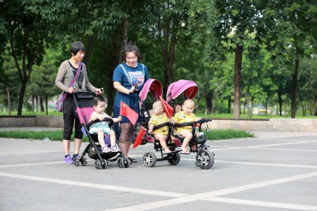 Photo for Luannan County, China - July 11, 2019: Two women pushed their babies for a walk in the park, Luannan County, Hebei Province, China - Royalty Free Image
