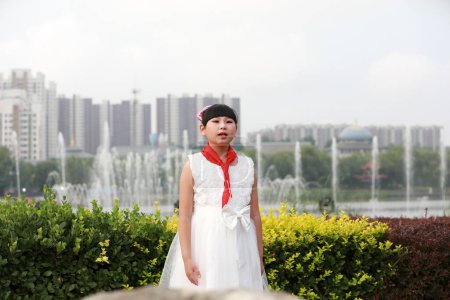 Photo for Luannan County, China - July 11, 2019: A little girl with a red scarf was singing aloud in the park, Luannan County, Hebei Province, China - Royalty Free Image