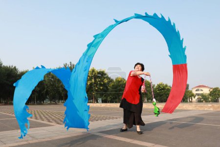 Téléchargez les photos : Comté de Luannan, Chine - 12 juillet 2019 : Des gens agitent des rubans pour faire de l'exercice dans les parcs, comté de Luannan, province du Hebei, Chine. De nos jours, beaucoup de Chinois attachent une grande importance à l'exercice physique. - en image libre de droit