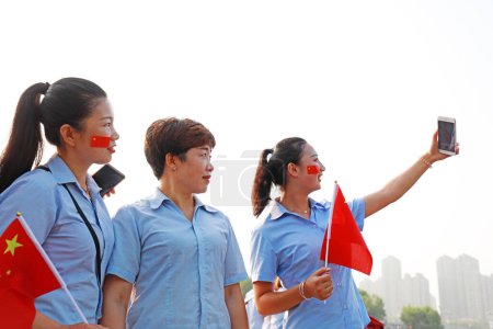 Foto de Condado de Luannan, China - 12 de julio de 2019: Las señoras están tomando fotos con la bandera nacional en la mano, Condado de Luannan, provincia de Hebei, China - Imagen libre de derechos