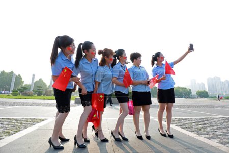 Foto de Condado de Luannan, China - 12 de julio de 2019: Las señoras están tomando fotos con la bandera nacional en la mano, Condado de Luannan, provincia de Hebei, China - Imagen libre de derechos