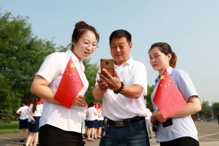 Photo for Luannan County, China - 12 July, 2019: People hold Chinese flags to check their mobile phones, Luannan County, Hebei Province, China - Royalty Free Image