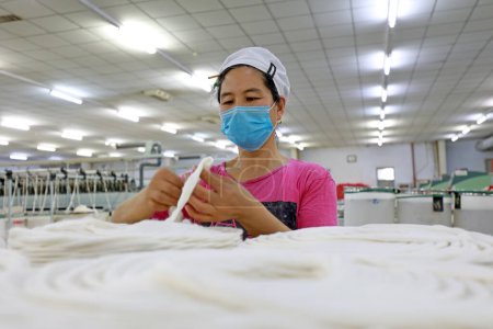 Foto de CONDADO DE LUANNAN, provincia de Hebei, China - 18 de marzo de 2020: La trabajadora está ocupada en la línea de producción en una fábrica de hilado. - Imagen libre de derechos