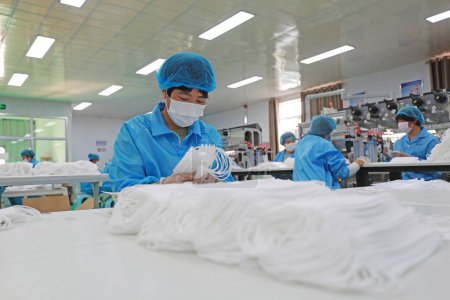 Téléchargez les photos : COMTÉ DE LUANNAN, province du Hebei, Chine - 15 avril 2020 : Les travailleurs sont occupés sur la ligne de production dans une usine de masques médicaux. - en image libre de droit