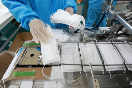 Téléchargez les photos : Les travailleurs sont occupés sur la ligne de production dans une usine de masques médicaux. - en image libre de droit