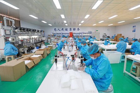 Foto de LUANNAN COUNTY, provincia de Hebei, China - 15 de abril de 2020: Los trabajadores están ocupados en la línea de producción en una fábrica de máscaras médicas. - Imagen libre de derechos