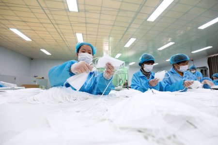 Foto de LUANNAN COUNTY, provincia de Hebei, China - 23 de abril de 2020: Los trabajadores están ocupados en la línea de producción en una fábrica de máscaras médicas. - Imagen libre de derechos
