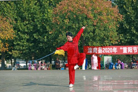 Téléchargez les photos : COMTÉ DE LUANNAN, Province du Hebei, Chine - 18 octobre 2020 : Une dame en rouge pratique l'épée tai chi sur la place - en image libre de droit