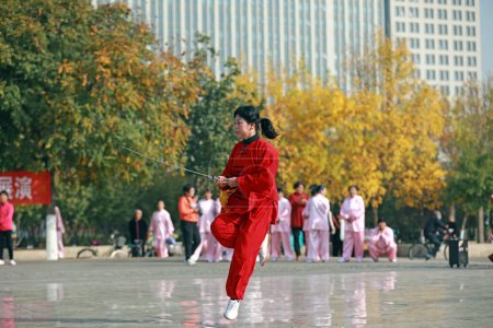 Foto de LUANNAN COUNTY, provincia de Hebei, China - 18 de octubre de 2020: Una dama de rojo practica la espada tai chi en la plaza - Imagen libre de derechos