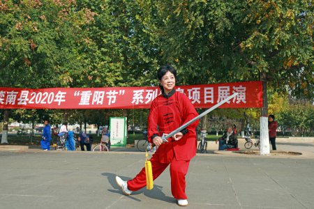 Foto de LUANNAN COUNTY, provincia de Hebei, China - 18 de octubre de 2020: Una dama de rojo practica la espada tai chi en la plaza - Imagen libre de derechos