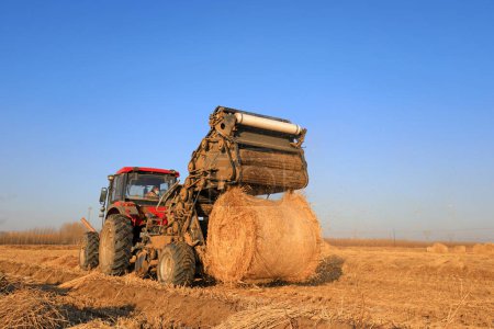 Foto de LUANNAN COUNTY, China - 24 de diciembre de 2020: los agricultores utilizan maquinaria agrícola para comprimir paja de arroz y empaquetarla en una granja, LUANNAN COUNTY, Hebei Province, China - Imagen libre de derechos