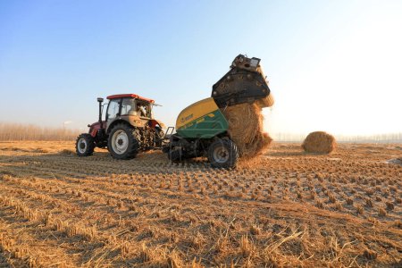 Foto de LUANNAN COUNTY, China - 25 de diciembre de 2020: los agricultores utilizan maquinaria agrícola para comprimir paja de arroz y empaquetarla en una granja, LUANNAN COUNTY, Hebei Province, China - Imagen libre de derechos