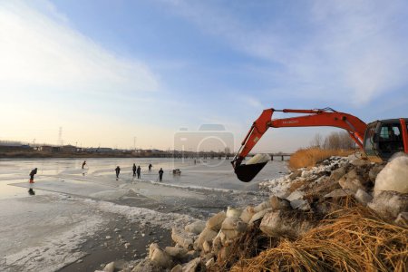 Photo for LUANNAN COUNTY, Hebei Province, China - January 22, 2021: Farmers use excavators to load canal ice in the wild, North China. - Royalty Free Image