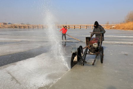 Foto de CONDADO DE LUANNAN, provincia de Hebei, China - 22 de enero de 2021: Los agricultores utilizan sierras eléctricas para cortar el hielo del río en la naturaleza - Imagen libre de derechos