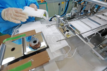Foto de Los trabajadores están ocupados en la línea de producción en una fábrica de máscaras médicas. - Imagen libre de derechos