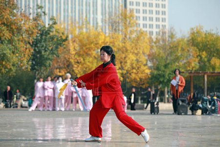 Photo for LUANNAN COUNTY, Hebei Province, China - October 18, 2020: A lady in red is practicing tai chi sword in the square - Royalty Free Image