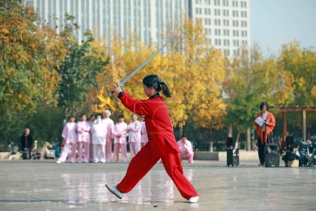 Photo for LUANNAN COUNTY, Hebei Province, China - October 18, 2020: A lady in red is practicing tai chi sword in the square - Royalty Free Image