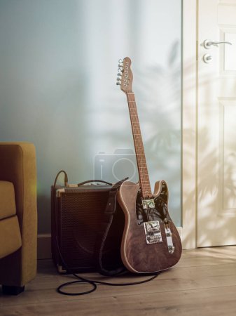 Téléchargez les photos : Guitare électrique et amplificateur debout sur le sol entre le canapé et la porte en plein soleil par la fenêtre - en image libre de droit