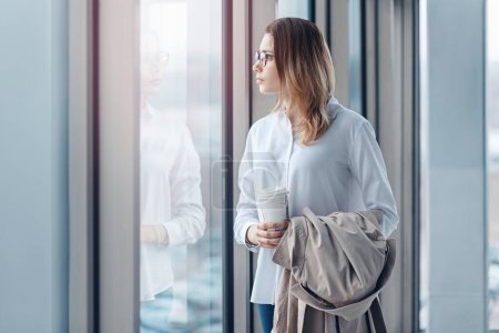 Photo for Young woman standing at the window of a modern office with a cup of coffee. - Royalty Free Image