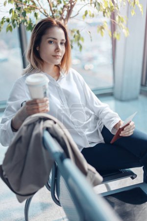 Foto de Mujer joven con tarjeta de embarque y pasaporte esperando un vuelo en la sala de embarque de un aeropuerto. - Imagen libre de derechos