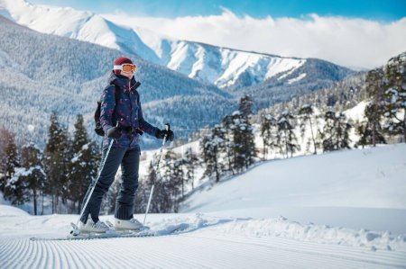 Téléchargez les photos : Skieuse amateur profitant de la vue sur les montagnes sur la pente de velours par une journée ensoleillée dans une station de ski. - en image libre de droit