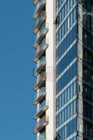 Téléchargez les photos : Détail d'un immeuble résidentiel moderne en verre, acier et béton contre un ciel bleu clair. - en image libre de droit