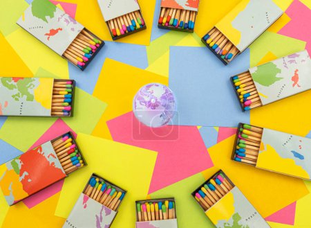 Téléchargez les photos : Un globe de terre cristalline entouré de boîtes d'allumettes carte du monde avec des bâtons colorés sur un fond de notes collantes en papier multicolore - en image libre de droit