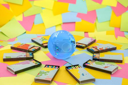 Téléchargez les photos : Un globe de terre cristalline entouré de boîtes d'allumettes avec des bâtons colorés sur un fond de notes collantes en papier multicolore - en image libre de droit