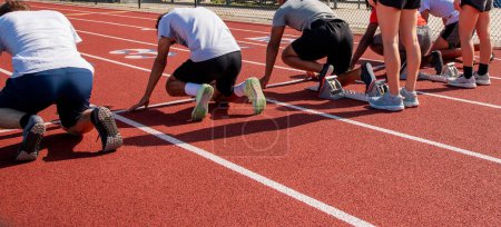 Photo for Reat view of high school sprint runners in the on your mark position ready to race each other in lanes on a track. - Royalty Free Image