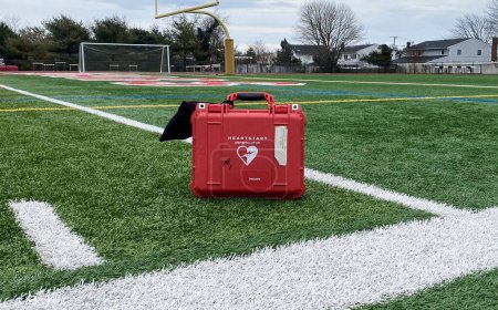 Téléchargez les photos : West Islip, New York, USA - 3 January 2023: One defibrillator machine, in a red case standing on a green turf football field. - en image libre de droit