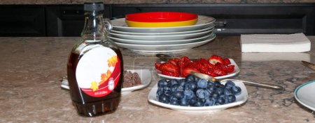 Photo for Fruit and chocolate chips on plates as toppings for waffles and pancakes set up on a kitchen counter with syrup. - Royalty Free Image