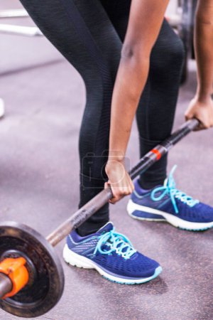 Téléchargez les photos : A high school female wearing spandex in the weight room lifitng a barbell with weights off the ground to clean it. - en image libre de droit