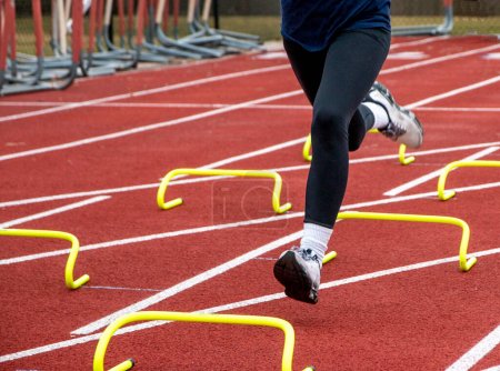 Photo for A runners legs wearing black spandex running over six inch yellow banana hurdles in lane on a track during practice. - Royalty Free Image