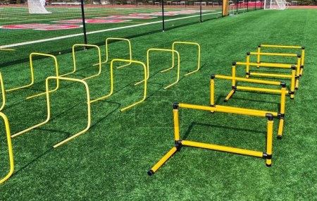 Three rows of plastic hurdles set up for athletes to jump over suring strength and agility practice on a green turf field.